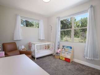 This charming nursery features a comfortable brown leather armchair, a white crib filled with plush toys, and a wooden bookshelf stocked with children's books.