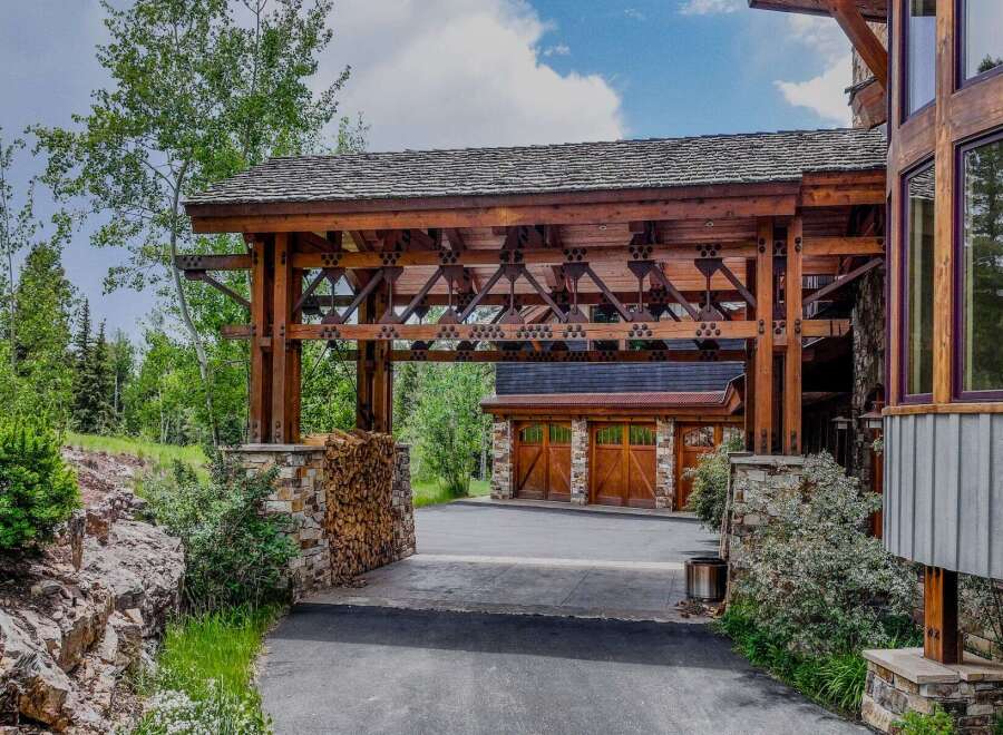 Experience rustic luxury with this stunning mountain home, featuring a grand porte-cochère with intricate wooden beams and stone accents.