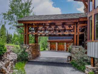 Experience rustic luxury with this stunning mountain home, featuring a grand porte-cochère with intricate wooden beams and stone accents.