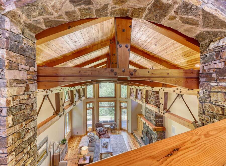 Experience rustic luxury in this stunning great room, featuring a soaring vaulted ceiling with exposed wooden beams and a magnificent stone fireplace.