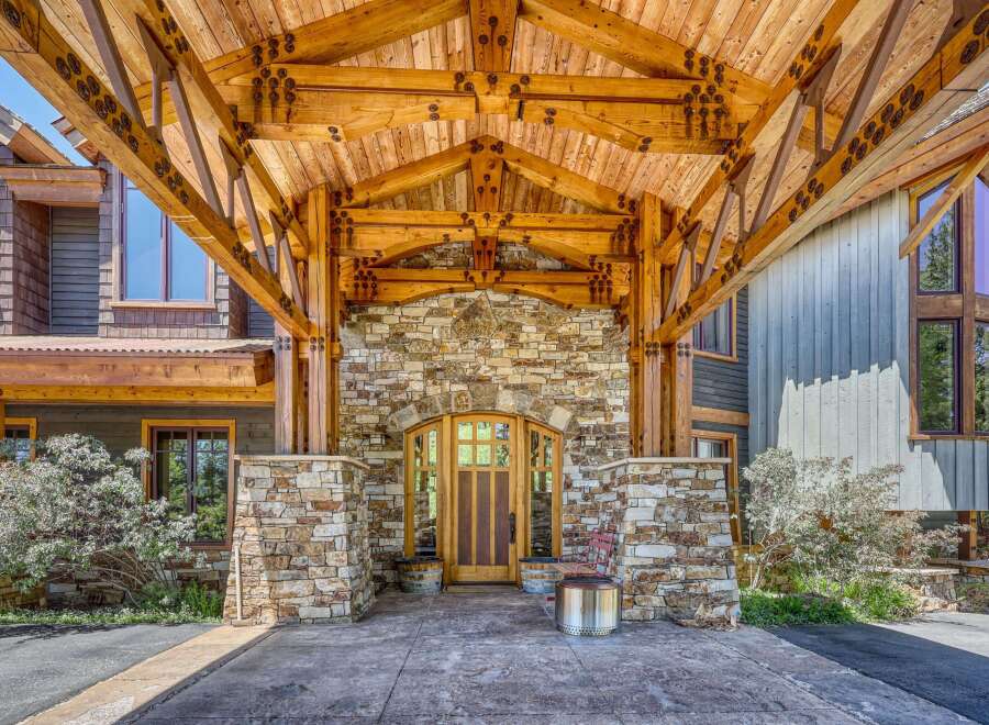 Experience rustic luxury with this stunning mountain home, featuring a grand covered entryway with exposed timber beams and natural stone accents.