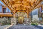 Experience rustic luxury with this stunning mountain home, featuring a grand covered entryway with exposed timber beams and natural stone accents.