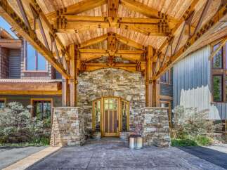 Experience rustic luxury with this stunning mountain home, featuring a grand covered entryway with exposed timber beams and natural stone accents.