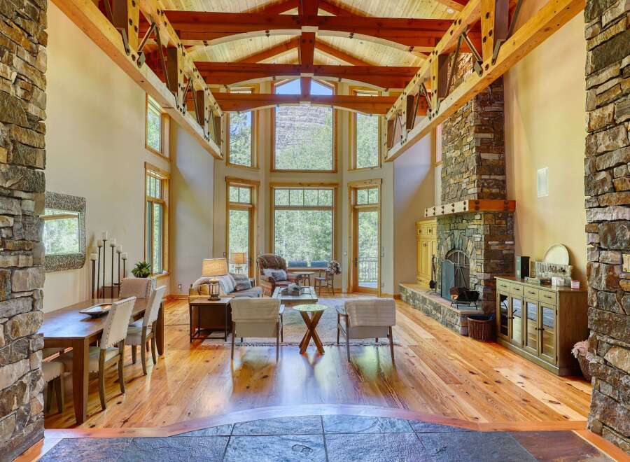 Experience rustic elegance in this stunning living space, featuring a grand stone fireplace and soaring vaulted ceilings with exposed wooden beams.