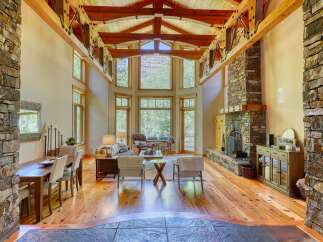 Experience rustic elegance in this stunning living space, featuring a grand stone fireplace and soaring vaulted ceilings with exposed wooden beams.