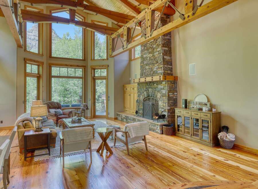 Experience breathtaking mountain views from this stunning living room, featuring a grand stone fireplace and soaring wooden beams.
