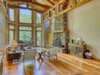 Experience breathtaking mountain views from this stunning living room, featuring a grand stone fireplace and soaring wooden beams.