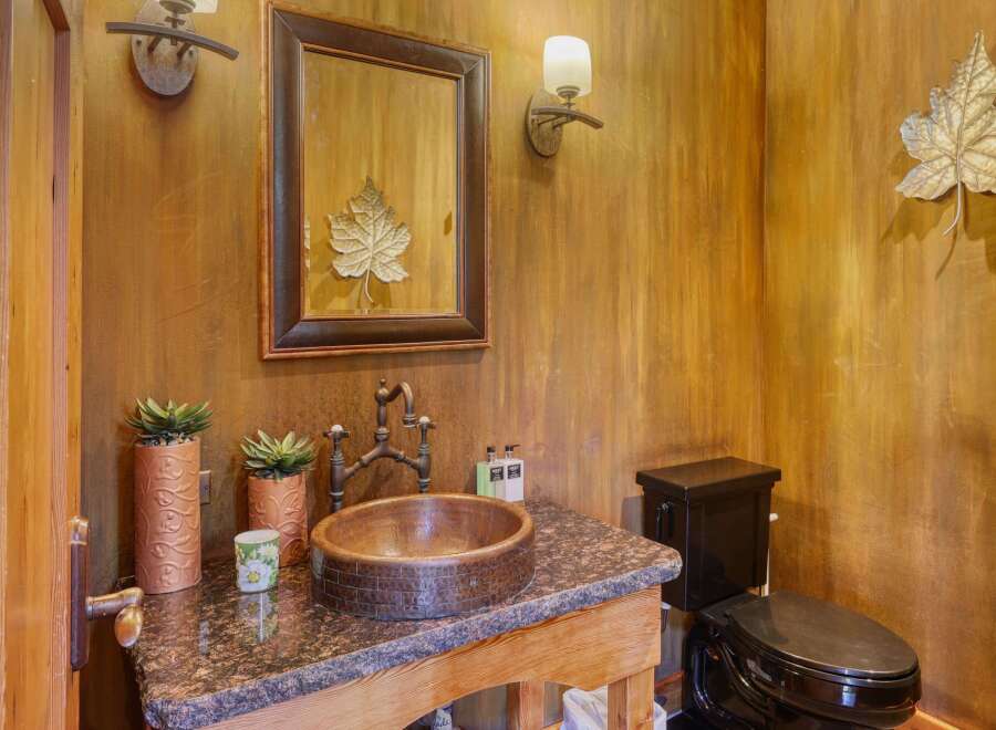 This rustic bathroom features a unique copper vessel sink with a vintage-style faucet, complemented by a dark granite countertop.