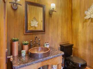 This rustic bathroom features a unique copper vessel sink with a vintage-style faucet, complemented by a dark granite countertop.