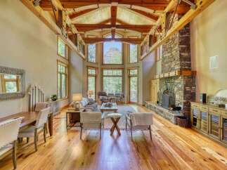 Experience breathtaking mountain views from this stunning living room, featuring a grand stone fireplace and soaring vaulted ceilings with exposed wooden beams.