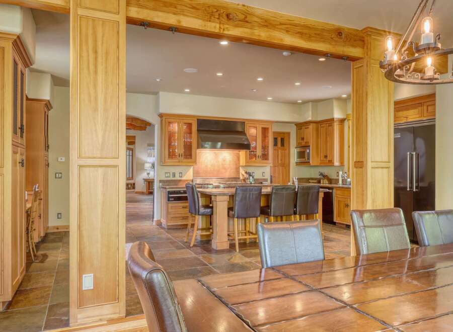 Experience luxury living in this stunning kitchen and dining area, featuring rich wood cabinetry, a spacious island with bar seating, and a grand chandelier.