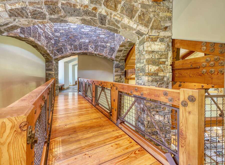 Experience rustic elegance in this stunning home featuring a unique stone archway leading to a charming wooden bridge.