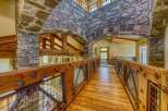 Experience rustic elegance in this stunning home featuring a grand wooden walkway with intricate metal railings and stone archways.