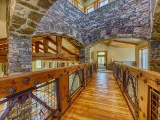 Experience rustic elegance in this stunning home featuring a grand wooden walkway with intricate metal railings and stone archways.