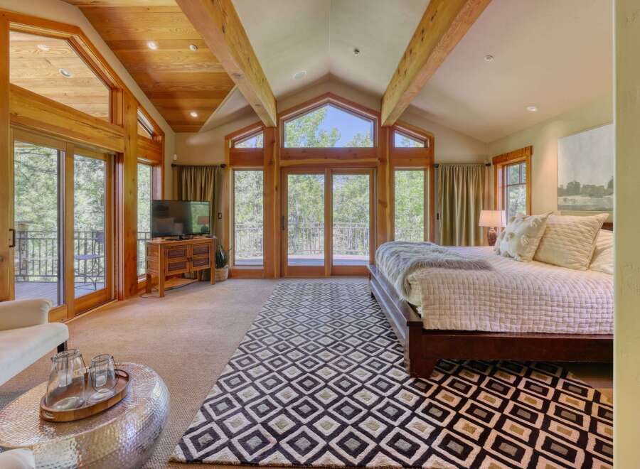 Experience luxury mountain living in this stunning bedroom featuring vaulted wood-beamed ceilings and expansive windows that flood the space with natural light.
