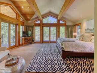 Experience luxury mountain living in this stunning bedroom featuring vaulted wood-beamed ceilings and expansive windows that flood the space with natural light.