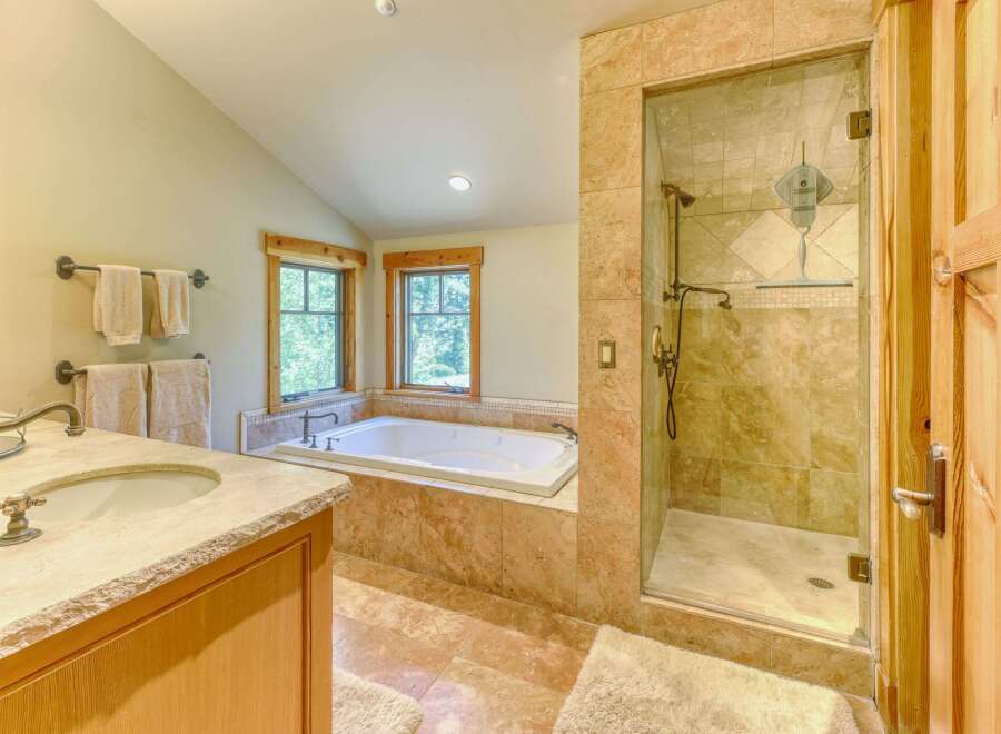 Experience luxury in this spacious bathroom featuring a deep soaking tub and a separate glass-enclosed shower with elegant tilework.
