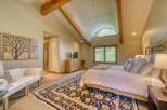 Experience rustic elegance in this spacious bedroom featuring vaulted ceilings with exposed wooden beams and a charming arched window offering serene views.