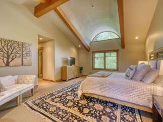 Experience rustic elegance in this spacious bedroom featuring vaulted ceilings with exposed wooden beams and a charming arched window offering serene views.