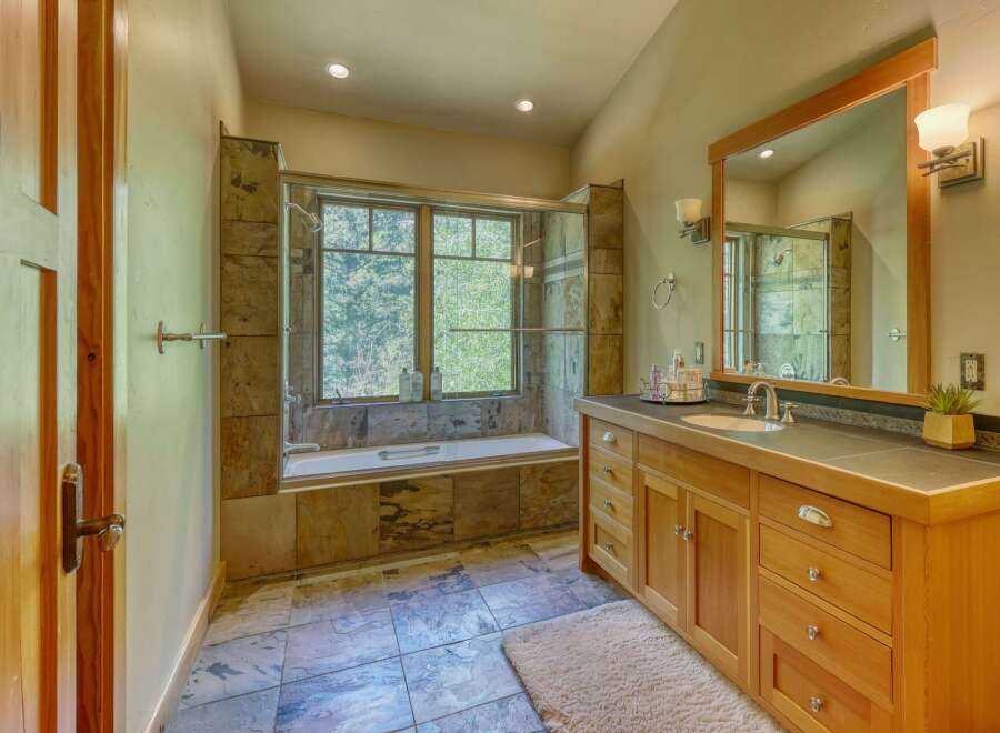 Experience luxury in this stunning bathroom featuring a deep soaking tub set against a backdrop of natural stone tile and a large window overlooking lush greenery.