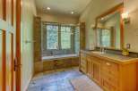 Experience luxury in this stunning bathroom featuring a deep soaking tub set against a backdrop of natural stone tile and a large window overlooking lush greenery.