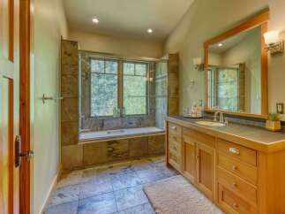 Experience luxury in this stunning bathroom featuring a deep soaking tub set against a backdrop of natural stone tile and a large window overlooking lush greenery.