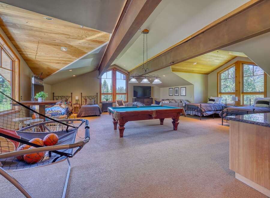 This spacious attic game room offers a perfect blend of entertainment and relaxation, featuring a pool table, arcade games, and multiple beds for guests.