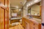 This rustic bathroom features a wooden vanity with a stone countertop and a stone-tiled shower/tub surround.