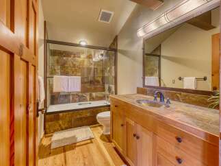 This rustic bathroom features a wooden vanity with a stone countertop and a stone-tiled shower/tub surround.