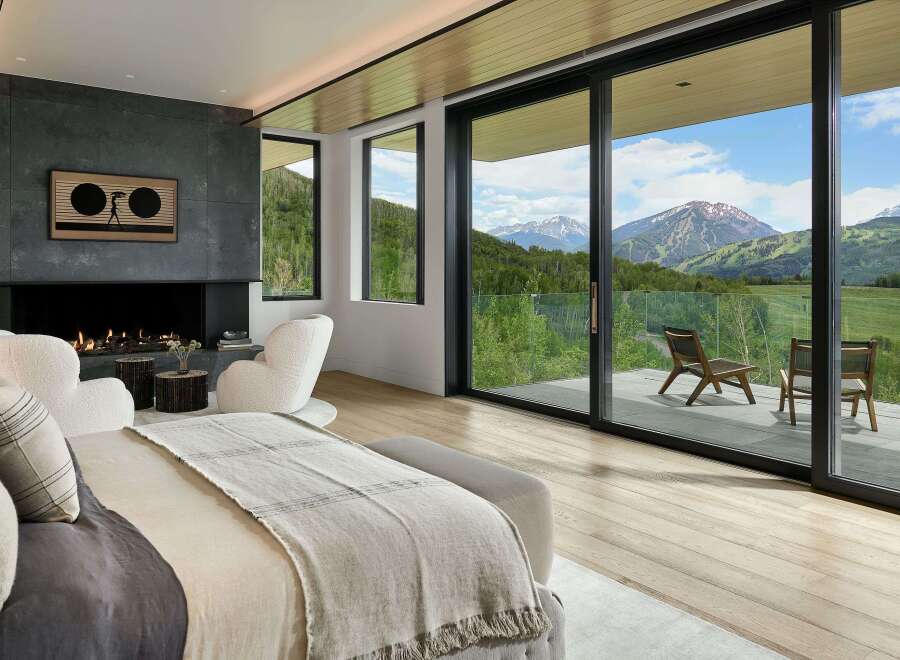 Experience luxury mountain living in this stunning bedroom featuring a modern fireplace and expansive sliding glass doors that open to breathtaking panoramic views.