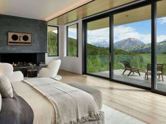 Experience luxury mountain living in this stunning bedroom featuring a modern fireplace and expansive sliding glass doors that open to breathtaking panoramic views.