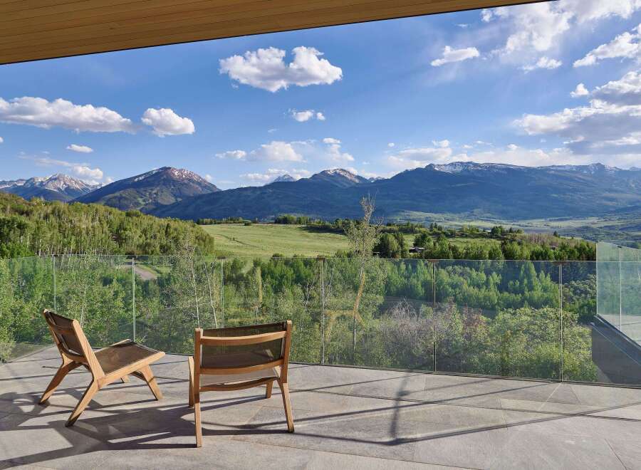 Experience breathtaking mountain views from this stunning modern home, featuring a spacious balcony with comfortable seating.