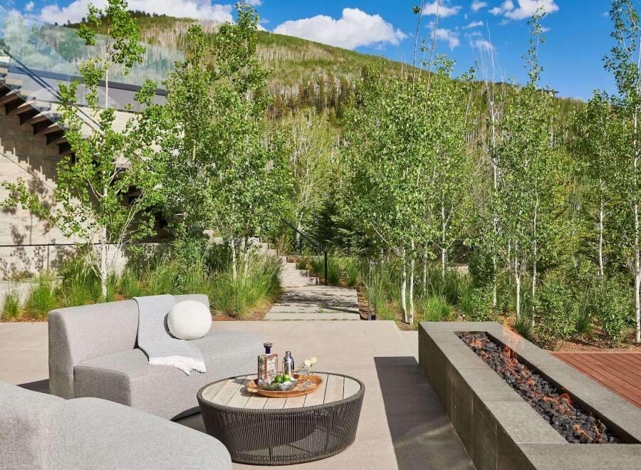 Experience luxury outdoor living with this stunning patio featuring a modern sectional sofa, a stylish coffee table with drinks, and a sleek linear gas fire pit.