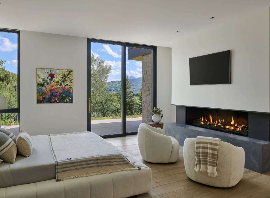 Experience luxury mountain living in this stunning bedroom featuring a modern gas fireplace and a large flat-screen TV.