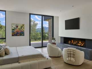Experience luxury mountain living in this stunning bedroom featuring a modern gas fireplace and a large flat-screen TV.