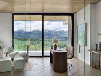 Experience breathtaking mountain views from this modern home office, featuring expansive glass walls and a sleek wooden desk.