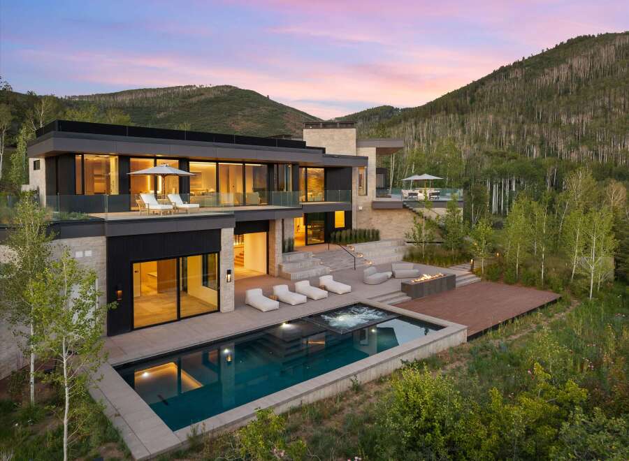 Experience luxury mountain living in this stunning modern home, featuring a sleek design with expansive glass walls and stone accents.