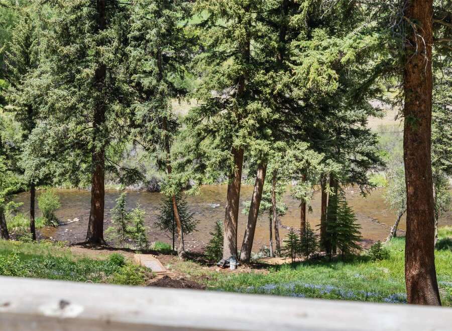 Experience serene living with this stunning property featuring a tranquil riverfront setting surrounded by lush evergreen trees.