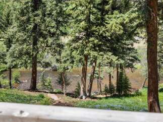 Experience serene living with this stunning property featuring a tranquil riverfront setting surrounded by lush evergreen trees.