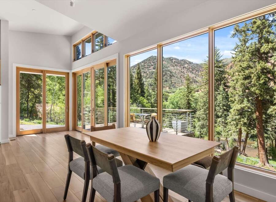 Experience breathtaking mountain and river views from this stunning dining area, featuring expansive windows and a modern wooden table.