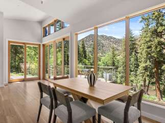Experience breathtaking mountain and river views from this stunning dining area, featuring expansive windows and a modern wooden table.