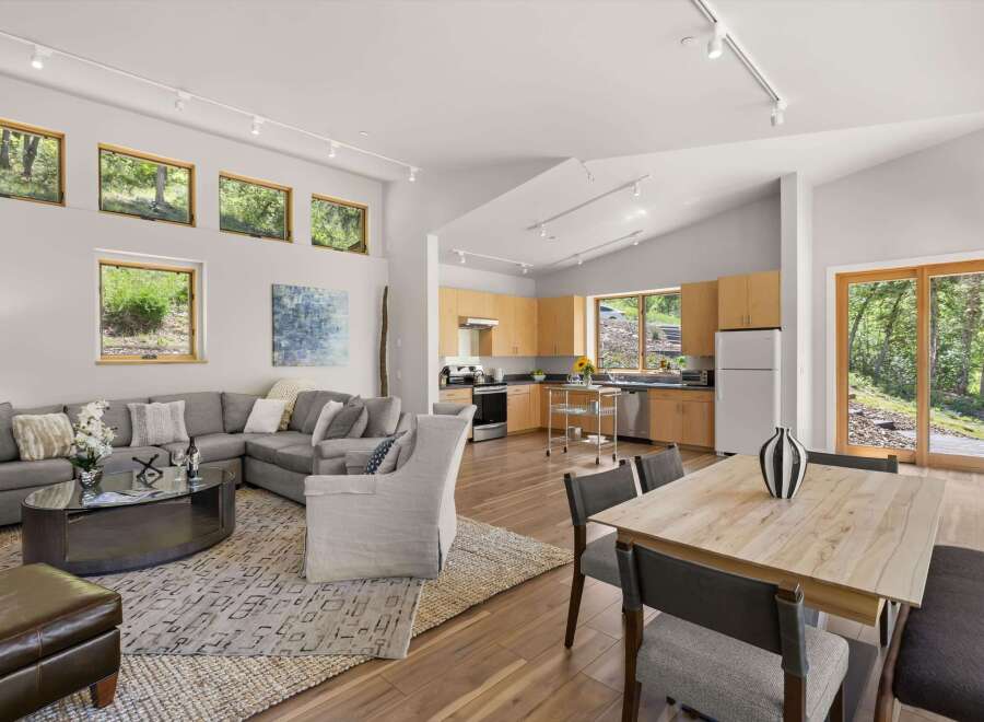Experience modern living in this open-concept home featuring a spacious living area with a sectional sofa and a stylish coffee table, seamlessly flowing into a well-equipped kitchen with light wood cabinetry.