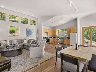 Experience modern living in this open-concept home featuring a spacious living area with a sectional sofa and a stylish coffee table, seamlessly flowing into a well-equipped kitchen with light wood cabinetry.