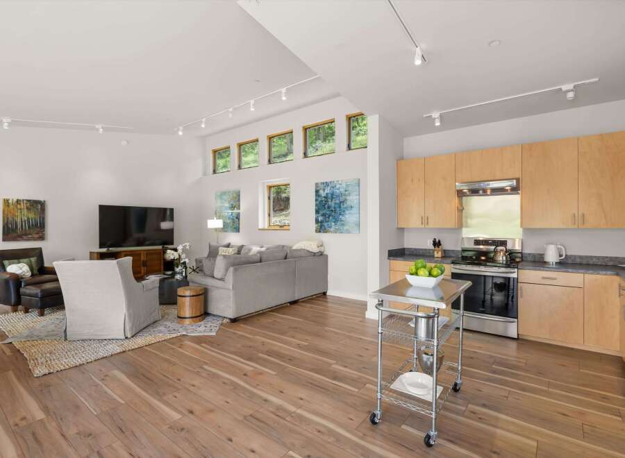 Experience modern living in this open-concept space featuring a sleek kitchen with light wood cabinetry and stainless steel appliances, seamlessly flowing into a bright living area.