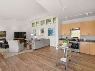 Experience modern living in this open-concept space featuring a sleek kitchen with light wood cabinetry and stainless steel appliances, seamlessly flowing into a bright living area.