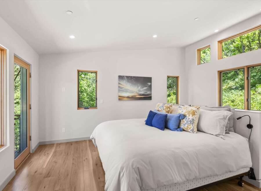 Experience serene living in this modern bedroom, featuring abundant natural light from large windows and a glass door, offering picturesque views of lush greenery.