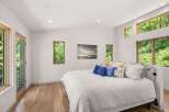 Experience serene living in this modern bedroom, featuring abundant natural light from large windows and a glass door, offering picturesque views of lush greenery.