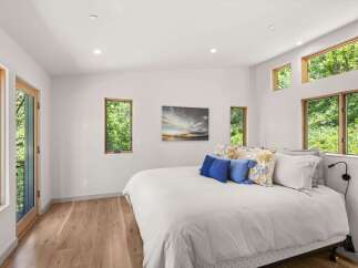 Experience serene living in this modern bedroom, featuring abundant natural light from large windows and a glass door, offering picturesque views of lush greenery.