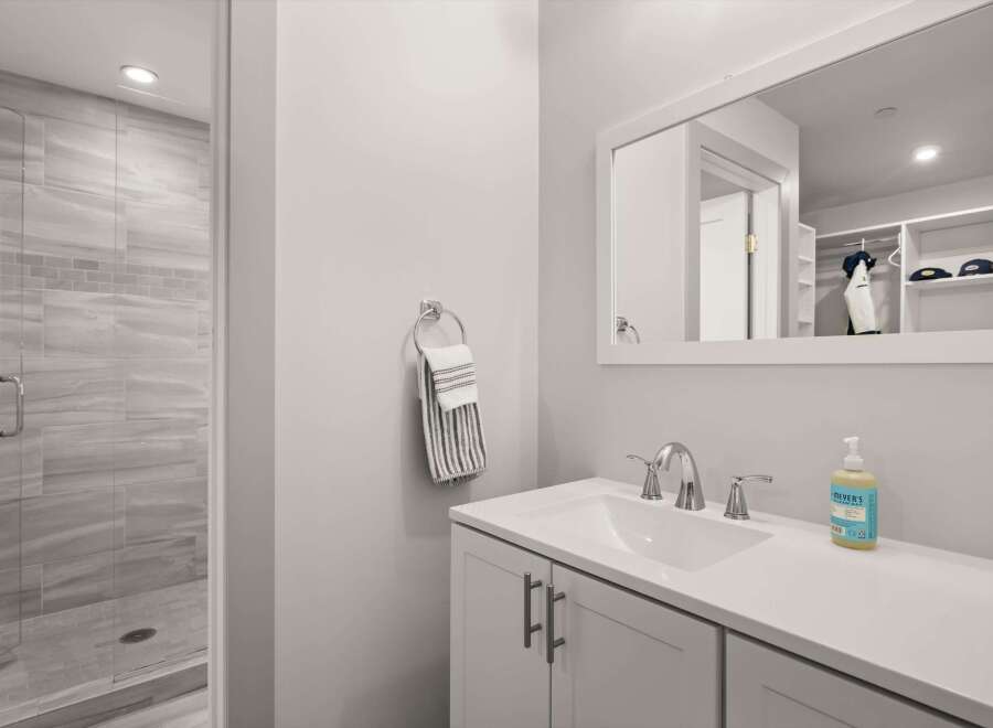 This modern bathroom features a sleek vanity with a white countertop and chrome fixtures, complemented by a spacious walk-in shower with elegant gray tilework.