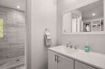 This modern bathroom features a sleek vanity with a white countertop and chrome fixtures, complemented by a spacious walk-in shower with elegant gray tilework.